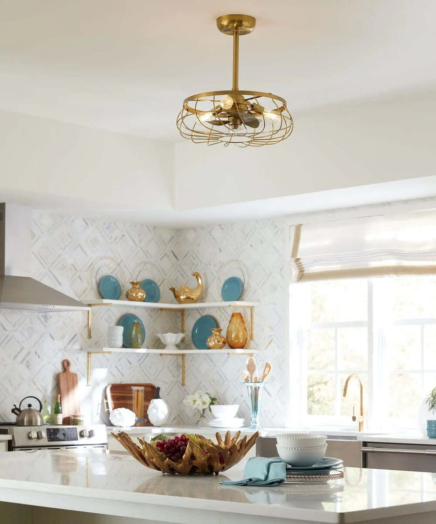 A gold color caged ceiling fan from Arranmore is pictured on a ceiling above a kitchen with an island and white backdrop.