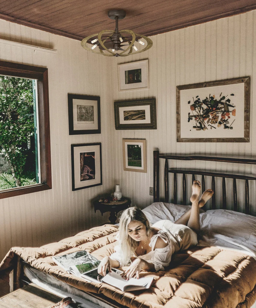 A women is pictured reading a book in a bed with pictures on the walls. An Arranmore caged fan is also pictured on the ceiling.